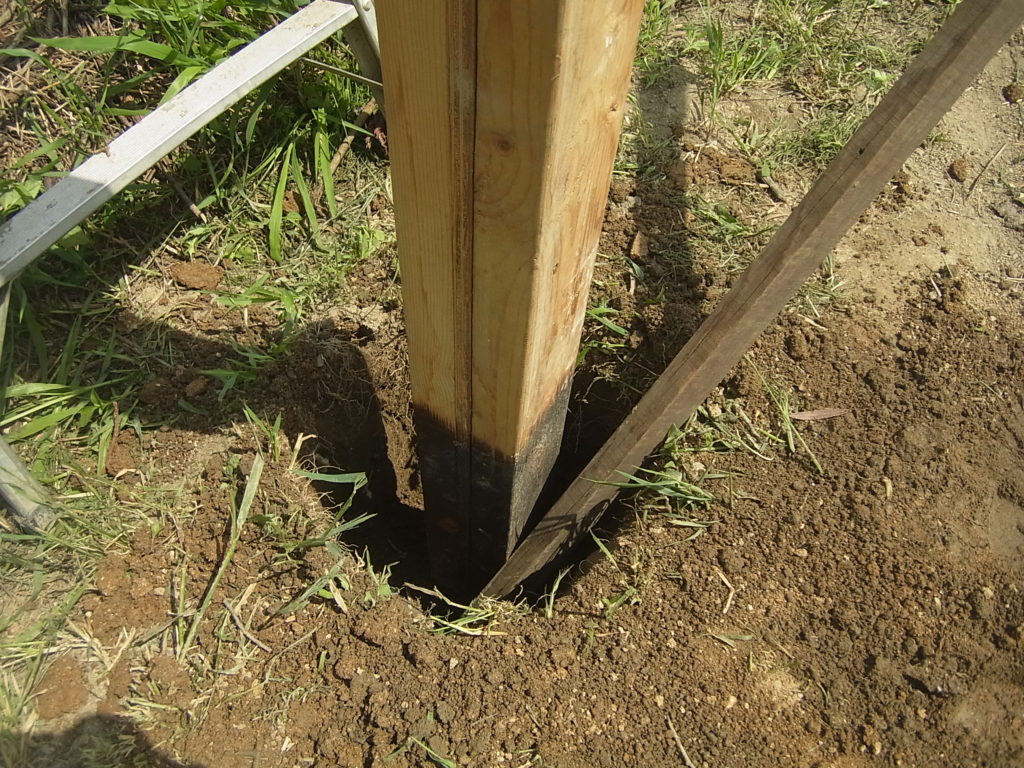 柱の周りの土を棒で突き固めていく。